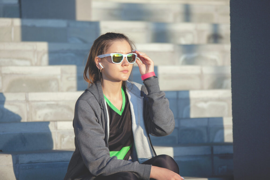 Woman sitting on steps in jogging gear and sports sunglasses
